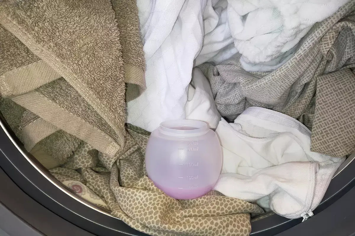 Un cestello pieno di biancheria, con un misurino di ammorbidente rosa. Si può mettere l'ammorbidente direttamente nel cestello per un bucato profumato.