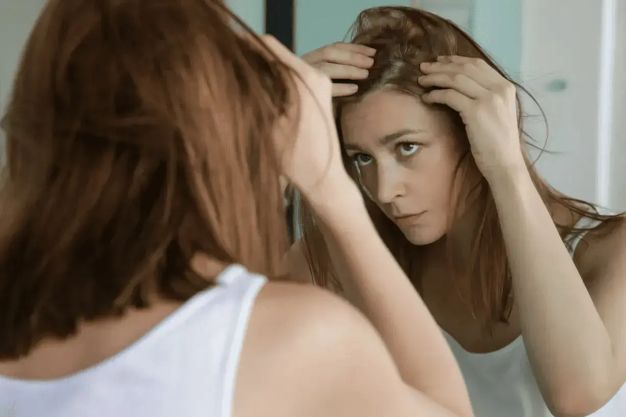 Mujer preocupada revisa su cuero cabelludo en el espejo, buscando soluciones sobre como frenar la caida del cabello.