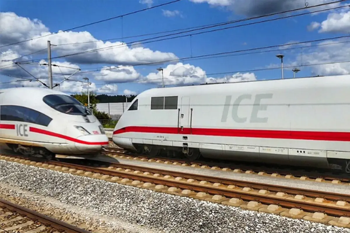 Zwei weiße ICE-Züge mit roten Streifen auf Gleisen, bereit für den Bahn Fernverkehr unter blauem Himmel mit Wolken.