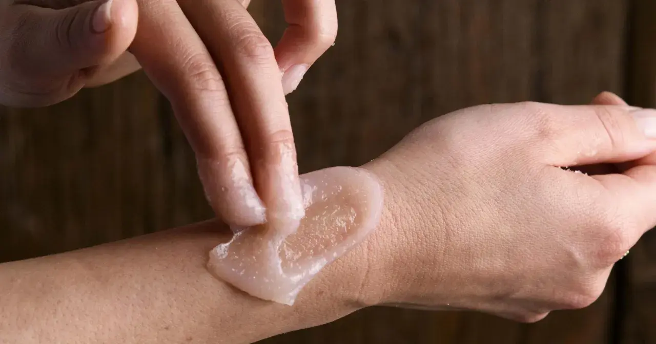 Mani che applicano scrub corpo sulla pelle. Per una pelle liscia, chiediti quante volte fare lo scrub corpo.