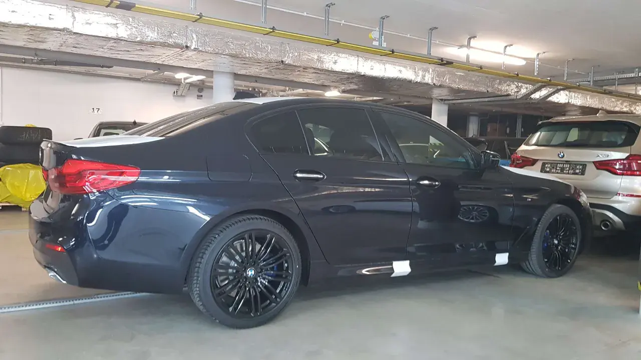 Ciemnogranatowe BMW 520d xDrive z czarnymi felgami stoi w garażu.