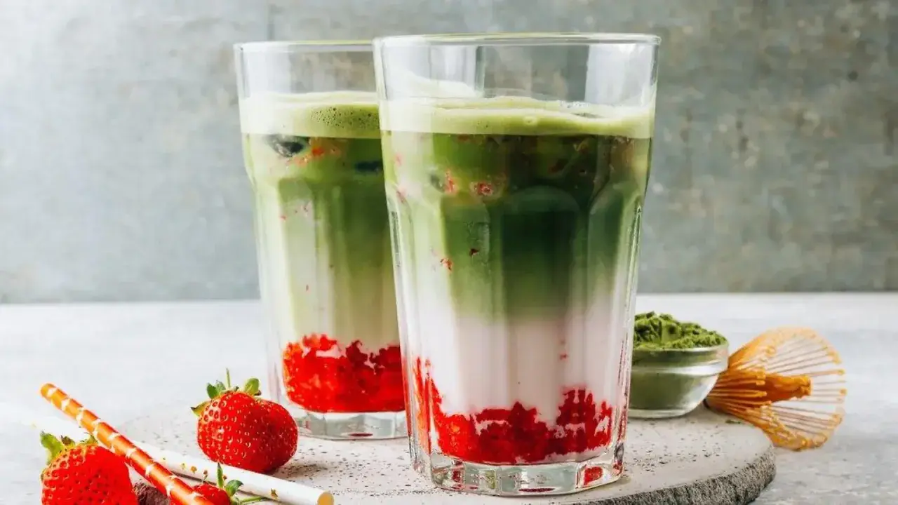 Zwei erfrischende Matcha-Erdbeer-Latte-Gläser mit Schichten aus Erdbeeren, Milch und leuchtend grünem Matcha.