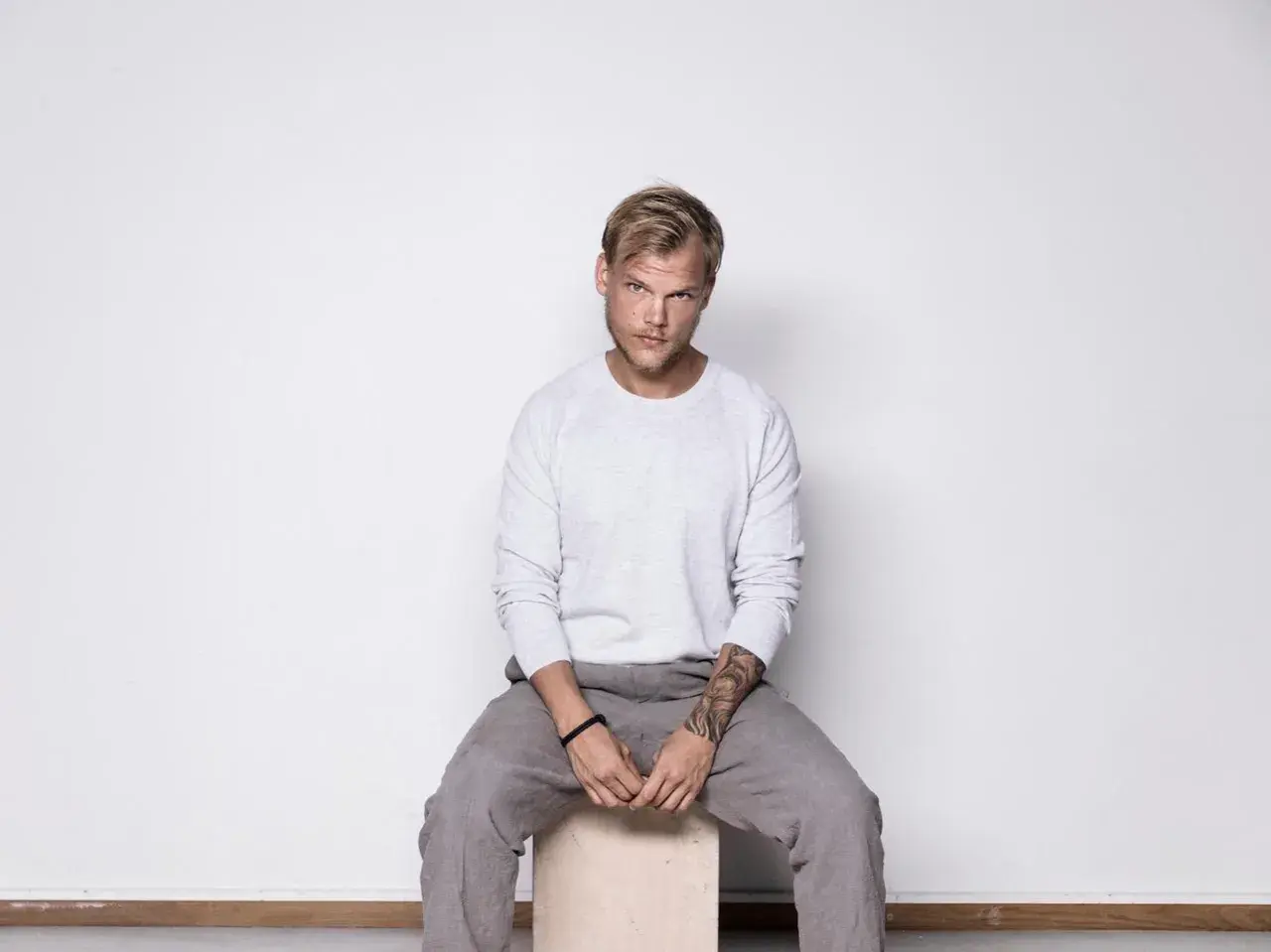 Avicii, siedzący na stołku, w szarym swetrze i spodniach. Jego śmierć wciąż budzi pytania.