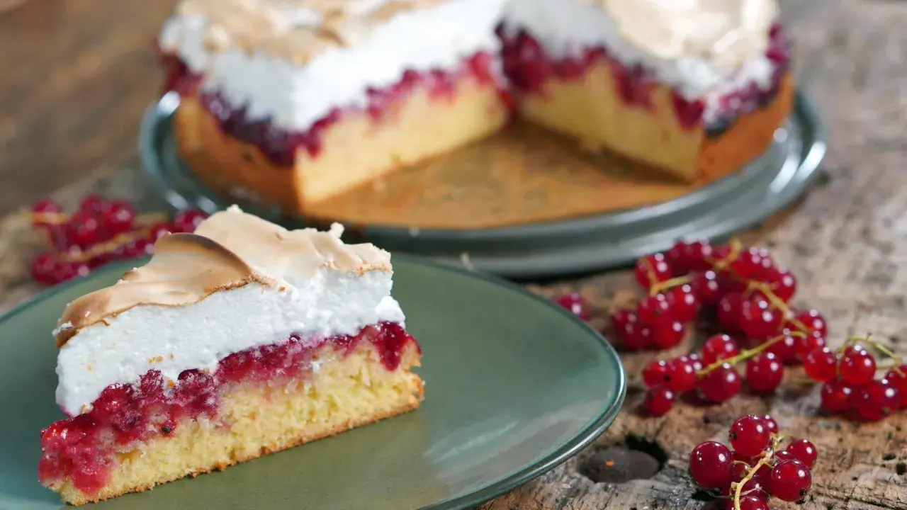 Ein saftiges Stück Johannisbeerkuchen mit Baiser, garniert mit frischen roten Johannisbeeren.