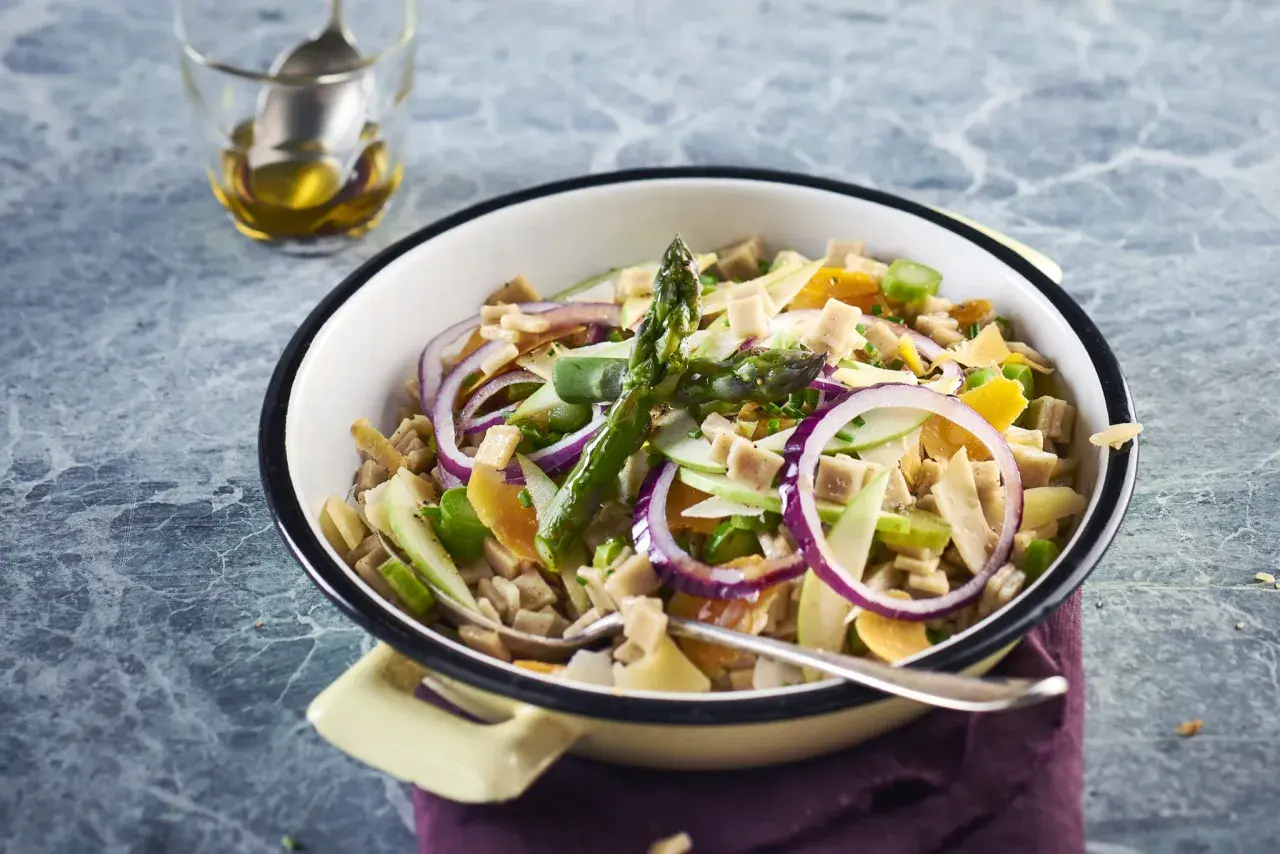 Salade de crozet colorée avec asperges, oignons rouges, pommes et dés de jambon, servie dans un plat émaillé.