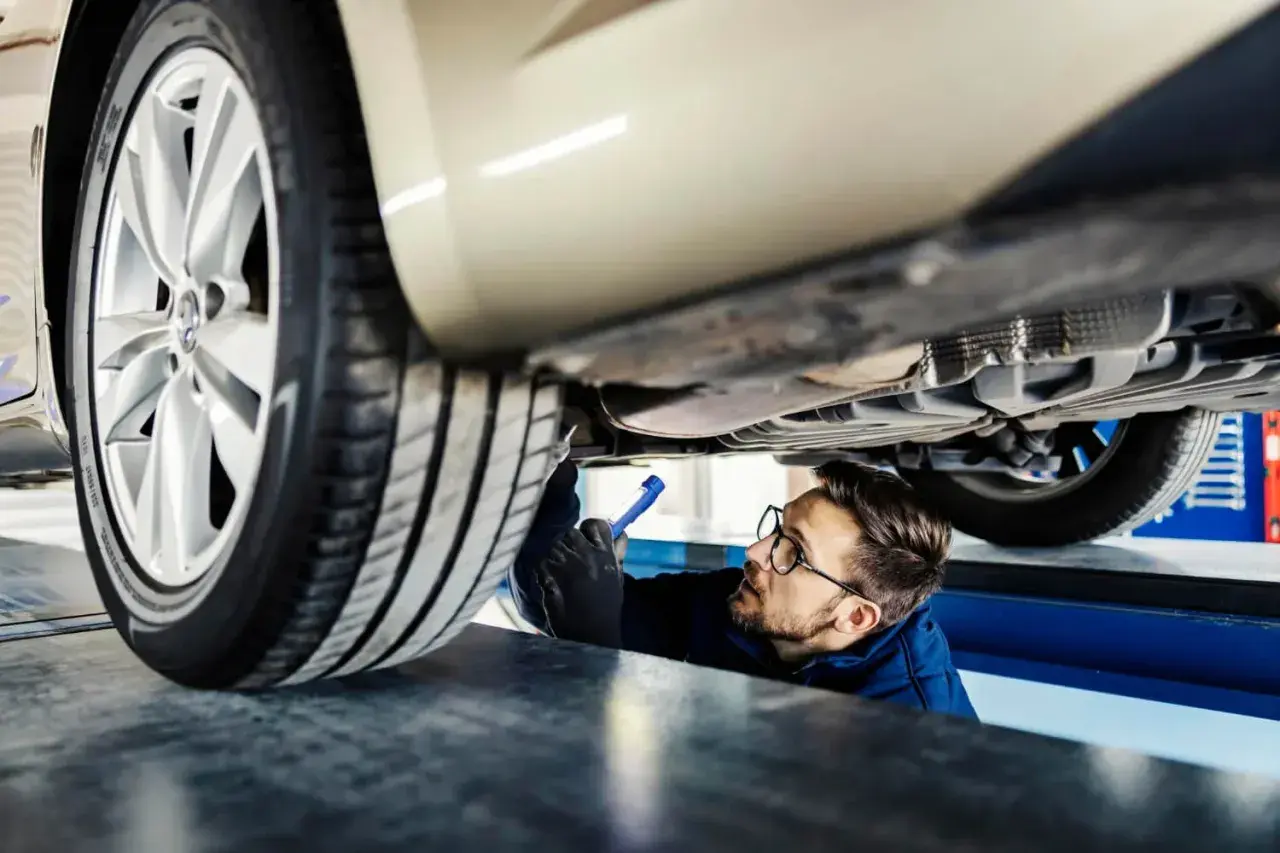 Mechanik z latarką bada podwozie samochodu.