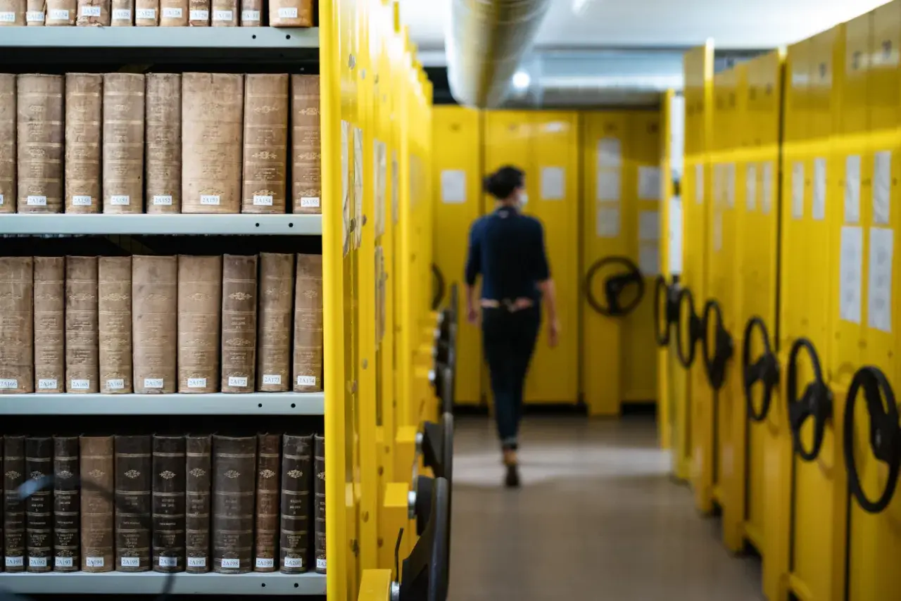 Rayons de livres anciens dans les archives départementales d'Indre-et-Loire en ligne, une personne se déplace dans l'allée.