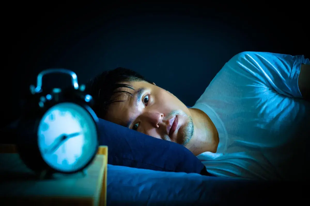 Hombre en cama, con ojos abiertos y alarma. Podría estar experimentando alucinaciones hipnagógicas.