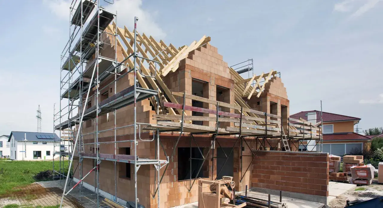 Rohbau firma im Einsatz: Ein Haus im Bau mit Gerüst, Ziegelwänden und Dachstuhl.