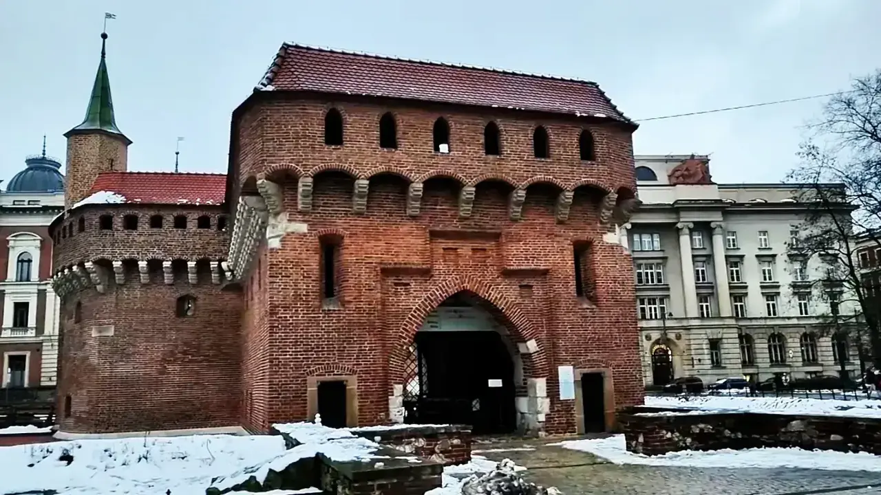 Imponujący barbakan kraków z cegły, z charakterystycznymi łukami i blankami, otoczony zimowym krajobrazem.