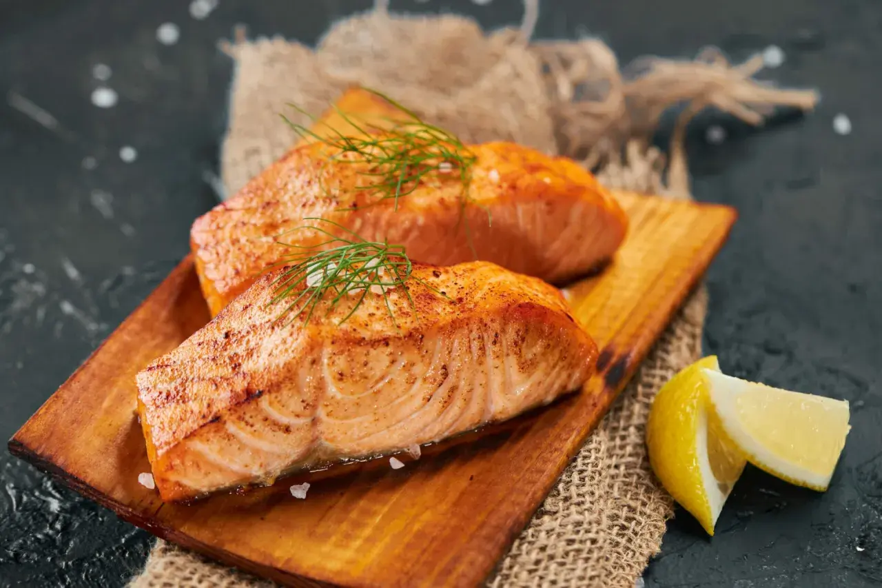 Deux pavés de saumon grillé, parsemés d'aneth et de gros sel, servis sur une planche en bois avec des quartiers de citron. Un délice pour accompagner un bon vin.