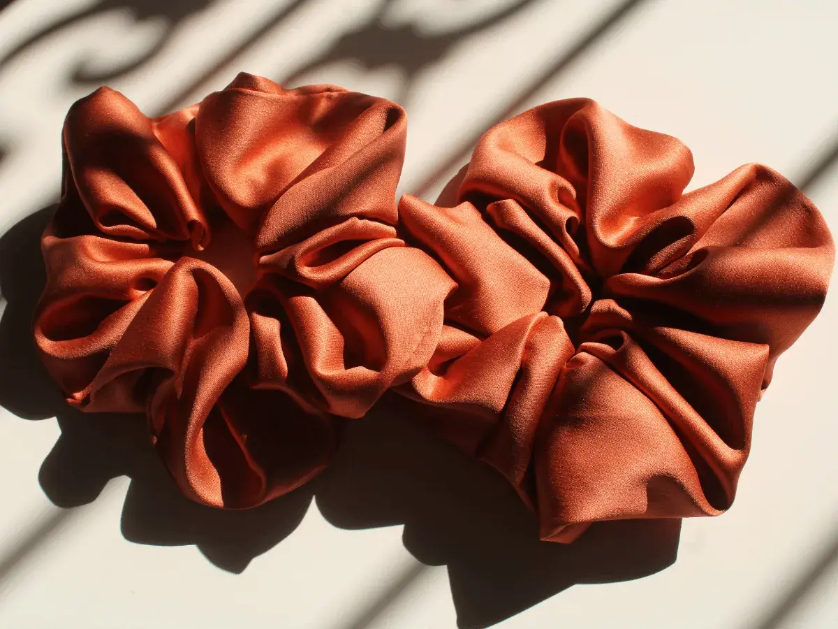 Dwa satynowe scrunchie w kolorze miedzianym, idealne do nauki, jak uszyć scrunchie.