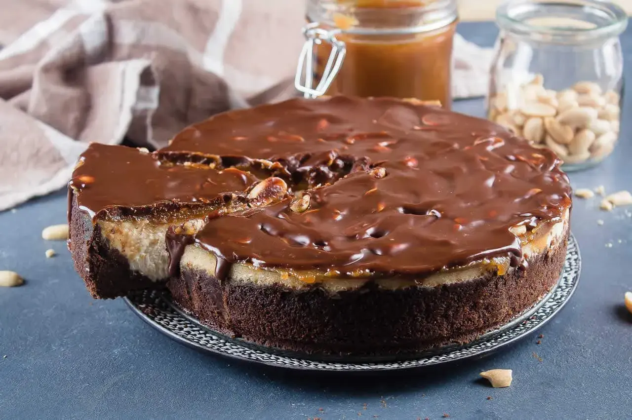 Gâteau façon Snickers, avec une base chocolatée, une couche crémeuse, du caramel coulant et une ganache au chocolat parsemée de cacahuètes. Un délice !