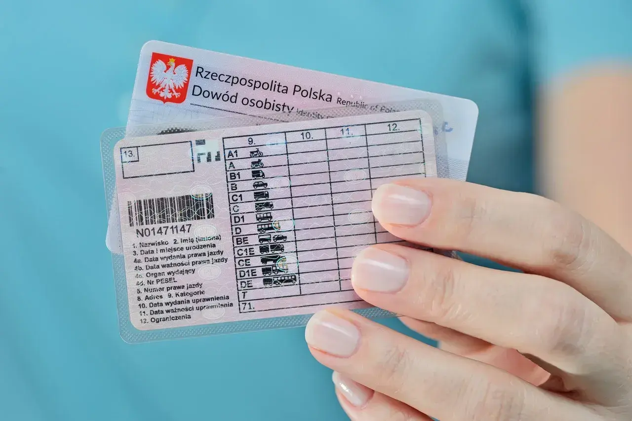 Dłoń trzyma polskie prawo jazdy z kategorią B, obok dowód osobisty.