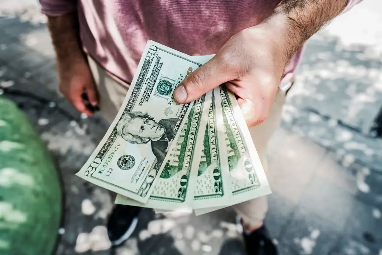 Dłoń trzyma kilka banknotów po 20 dolarów. Zastanawiasz się, skąd wziąć kasę na spełnienie marzeń?