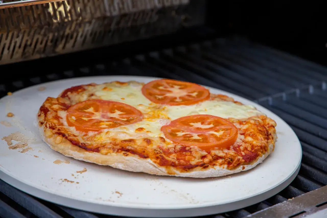Eine Margherita-Pizza mit Tomatenscheiben und geschmolzenem Käse wird auf einem Pizzastein im Backofen gebacken.