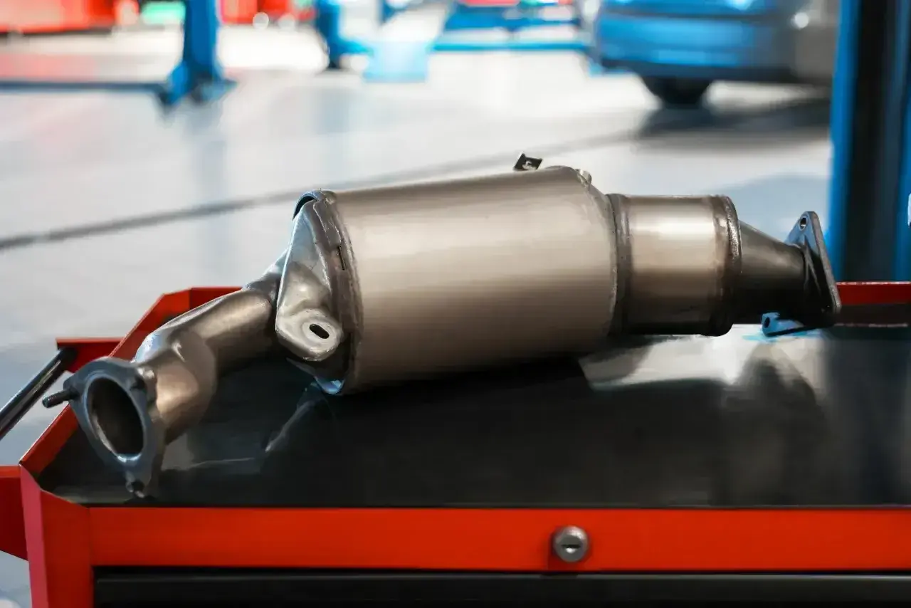 Nowy katalizator samochodowy, czyli GPF (Gasoline Particulate Filter), leży na wózku warsztatowym.