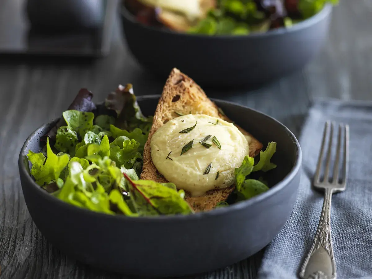 Salade fraîche avec une tranche de pain grillé et une quenelle de **chèvre chaud** garnie d'herbes.