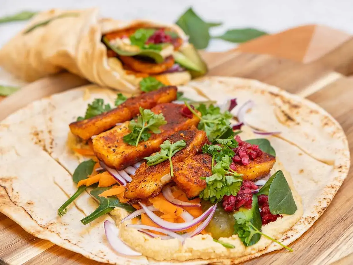 En läcker halloumi wrap med hummus, rivna morötter, rödlök och färska örter. En annan wrap syns i bakgrunden.