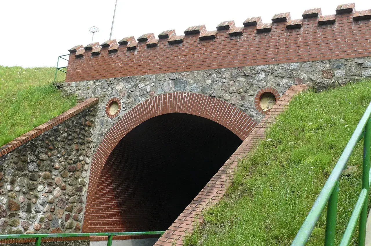 Akwedukt w Fojutowie, z ceglanym łukiem i kamiennym murem, otoczony zielenią.