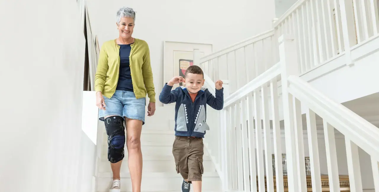 Frau mit Kniebandage, die mit ihrem Enkel die Treppe hinuntergeht. Einlagen bei Kniearthrose können helfen, die Mobilität zu verbessern.