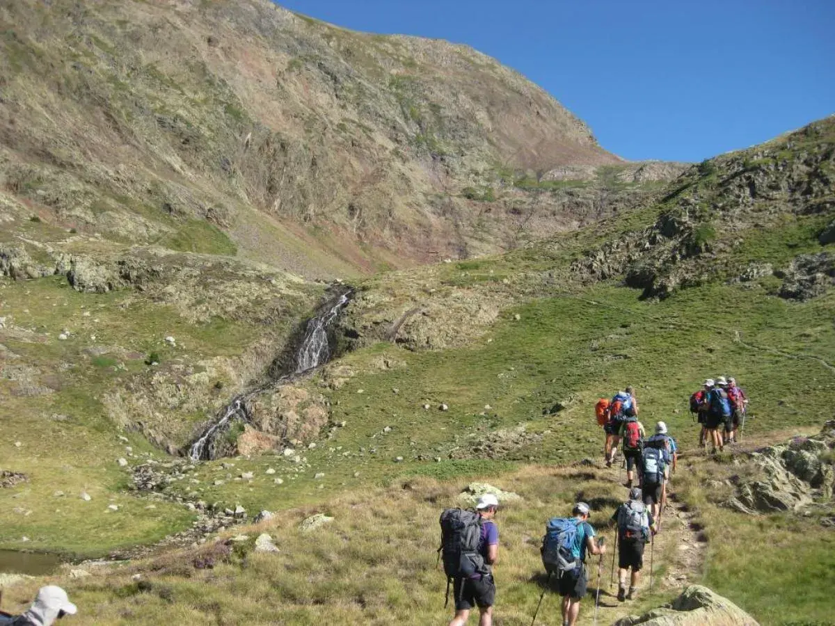Senderistas caminan por un sendero de montaña hacia una cascada, como si fuera la porta del cel.