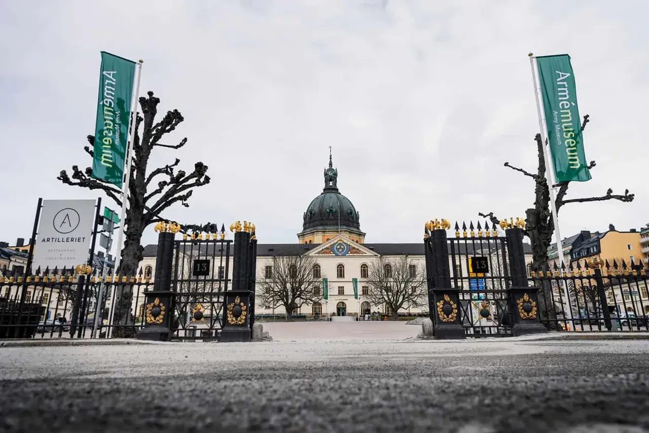 Grön flagga med texten "Armémuseum" vid krigsmuseum Stockholm. Imponerande byggnad med kupol och staket.