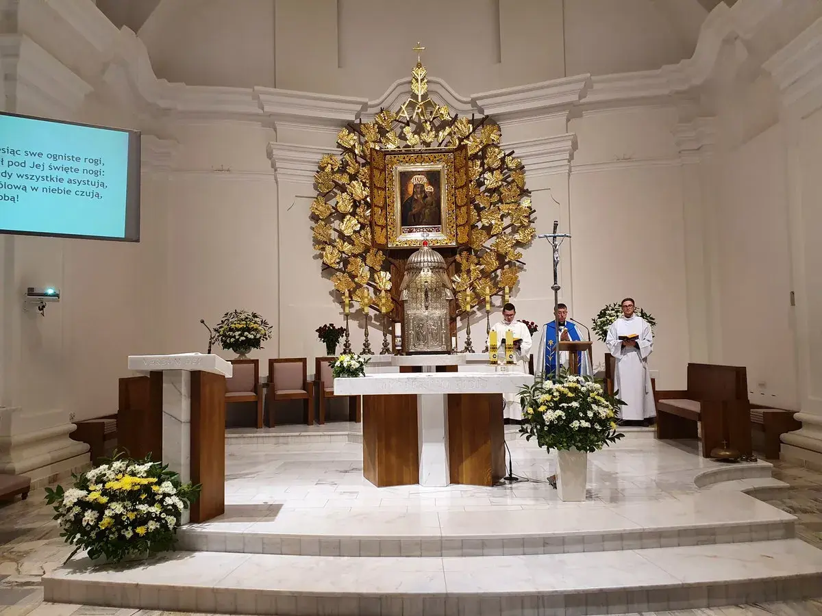 Msza w kościele w Dąbrówce Kościelnej. Trzech duchownych przy ołtarzu, ozdobionym złotym antepedium i obrazem Matki Boskiej.