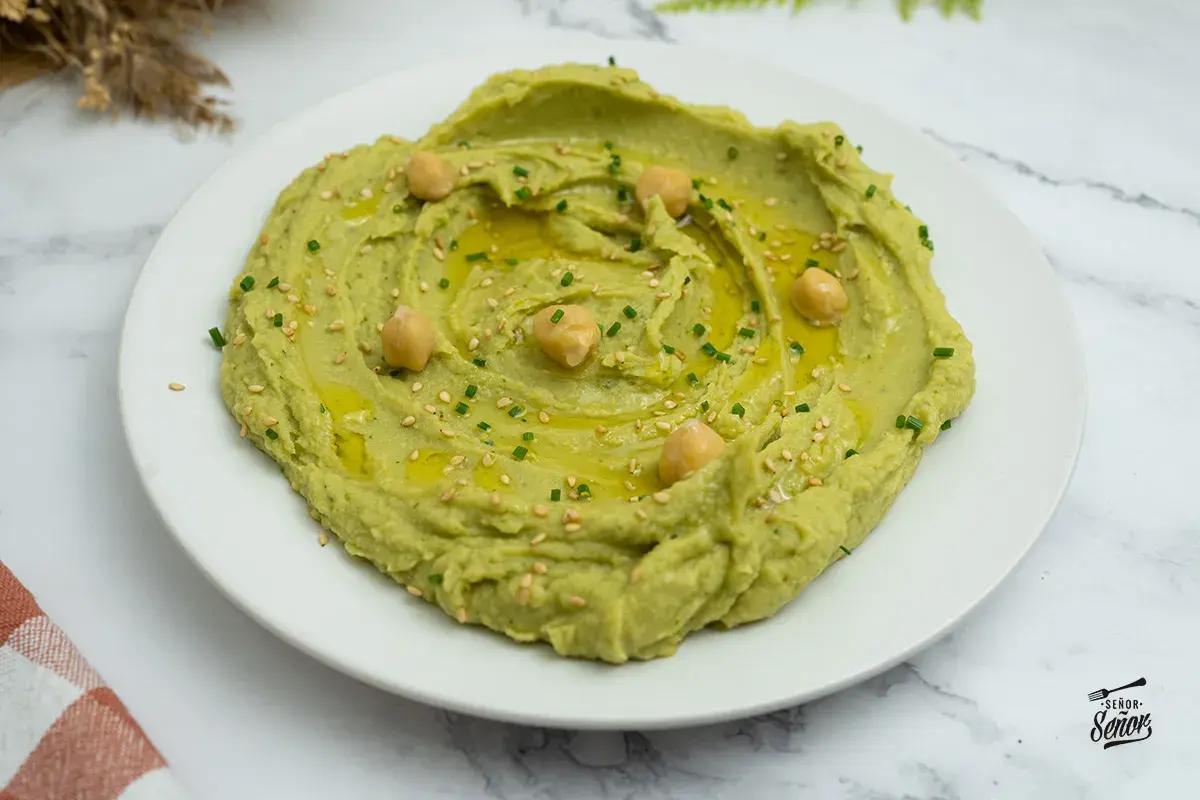 Hummus de aguacate cremoso, decorado con garbanzos, aceite de oliva, semillas de sésamo y cebollino. ¡Un entrante delicioso!