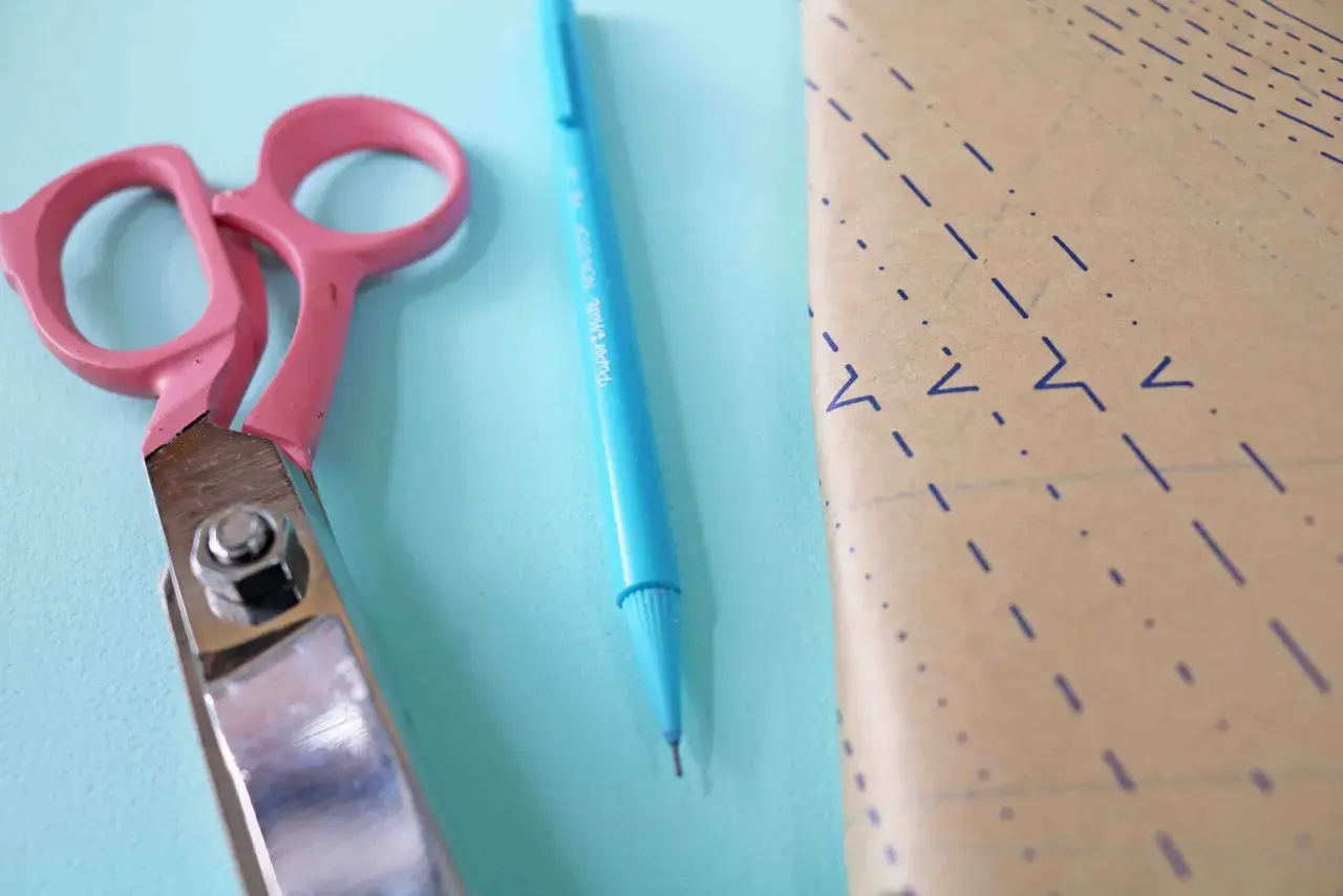 Pink scissors and a blue pen lie next to a piece of pattern paper, ready for a project to place on fold.