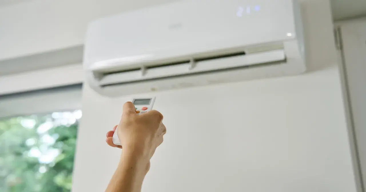 Dłoń trzymająca pilot do klimatyzacji, która chłodzi pomieszczenie. Zastanawiasz się, czy klimatyzacja pobiera dużo prądu?