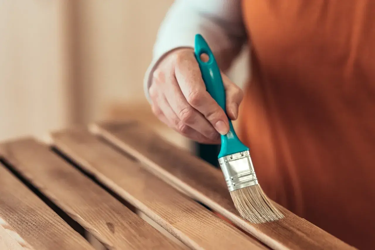 Mano con brocha lijando listones de madera barnizada para restaurar un mueble.