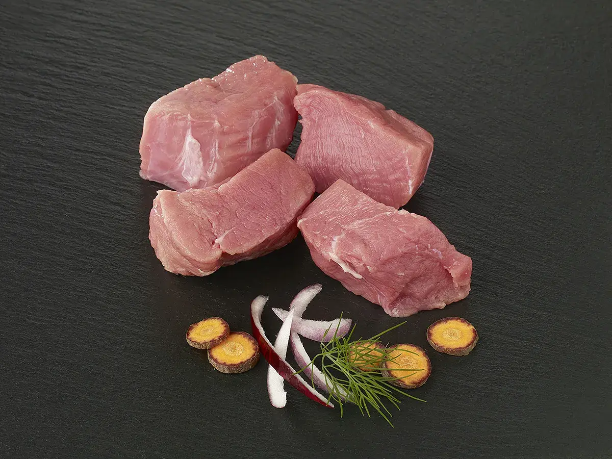 Quatre morceaux d'épaule de veau crus, accompagnés de rondelles de carottes, d'oignon rouge et d'aneth sur fond noir.