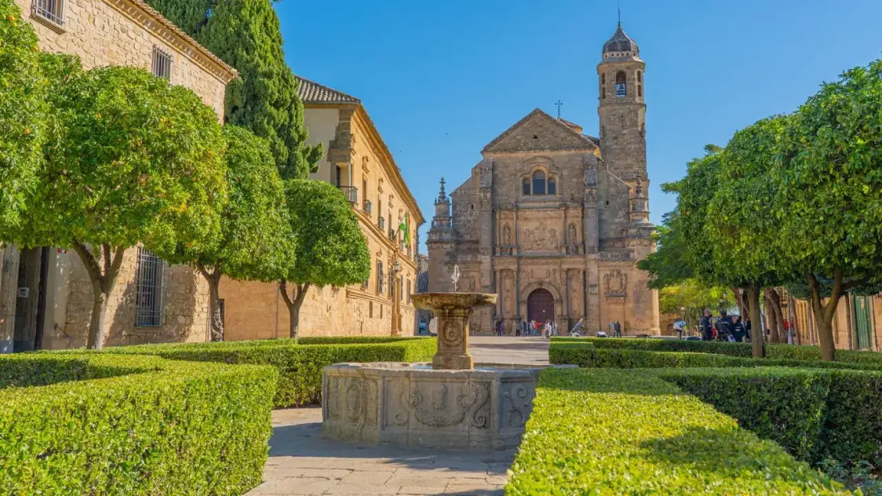 Fuente renacentista en plaza de Úbeda y Baeza, con iglesia barroca al fondo y árboles frutales.