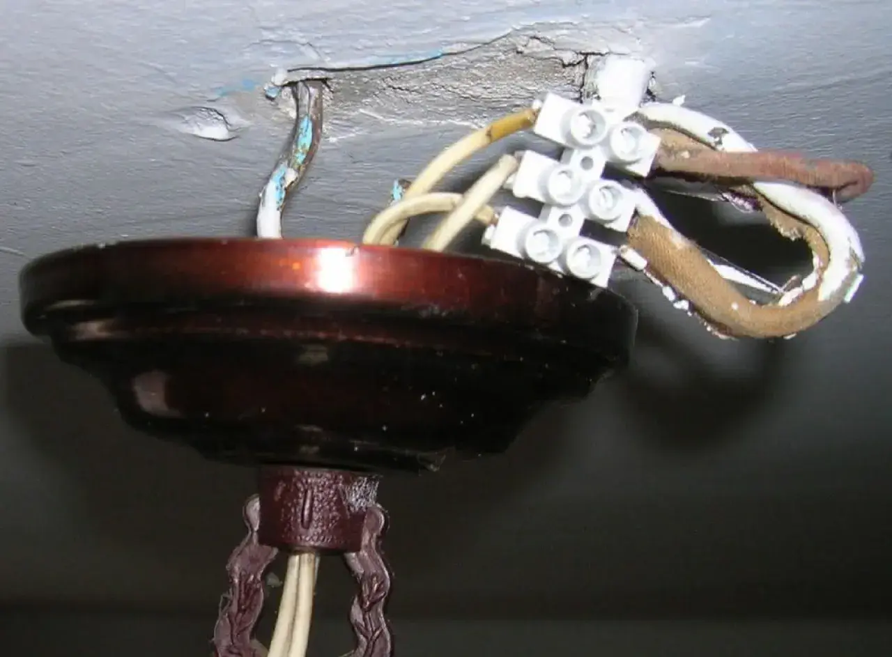 Podłączanie nowego żyrandola do starej instalacji: widoczne przewody i kostka elektryczna przy suficie.