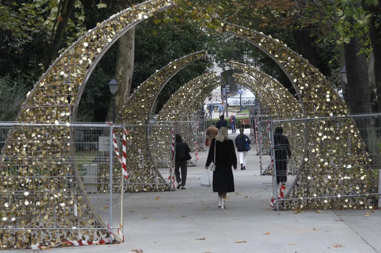 Personas pasean bajo arcos dorados decorados con luces, preparándose para el encendido de luces en Oviedo.