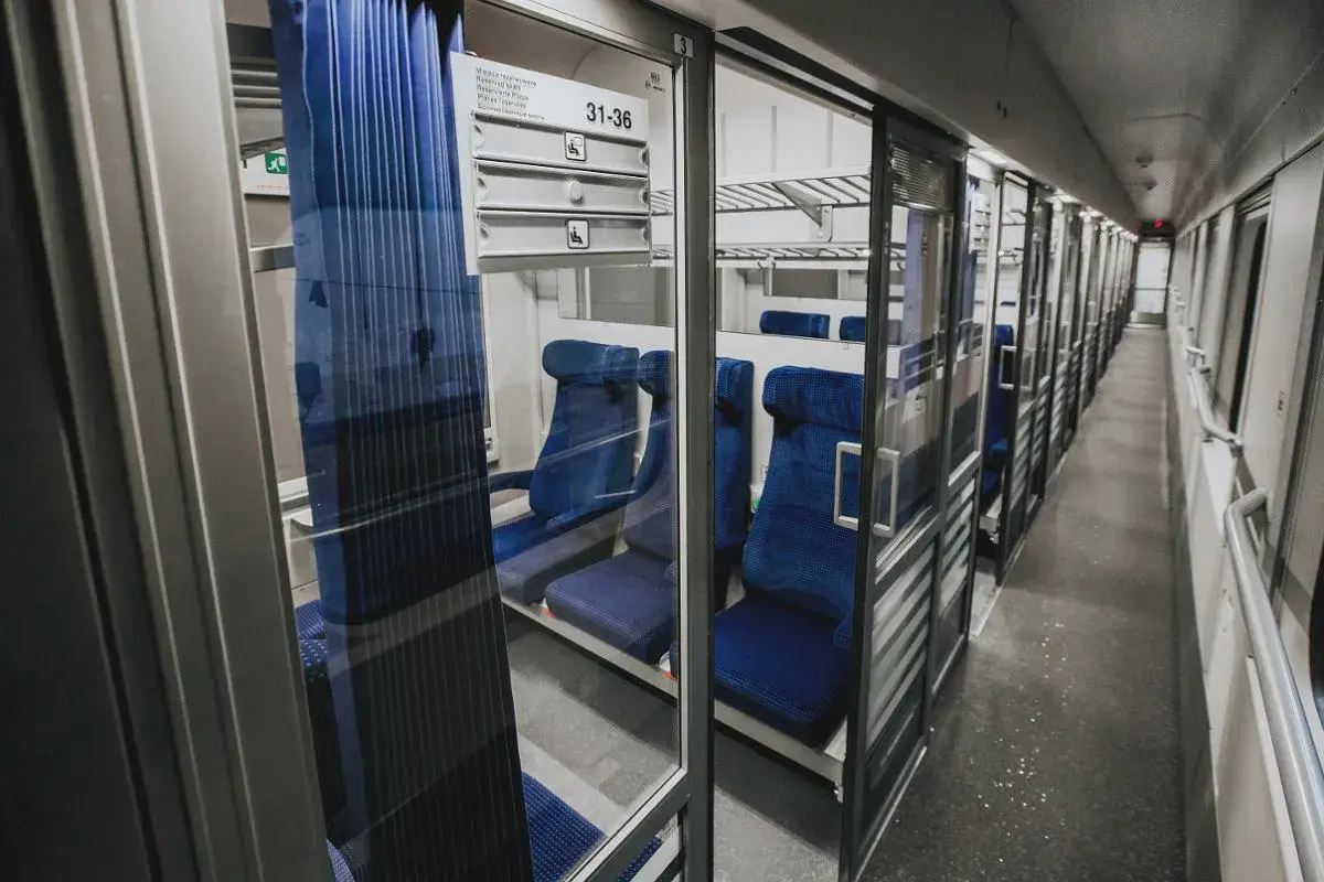 Wnętrze wagonu z przedziałami intercity 2 klasa. Puste, niebieskie siedzenia czekają na pasażerów.