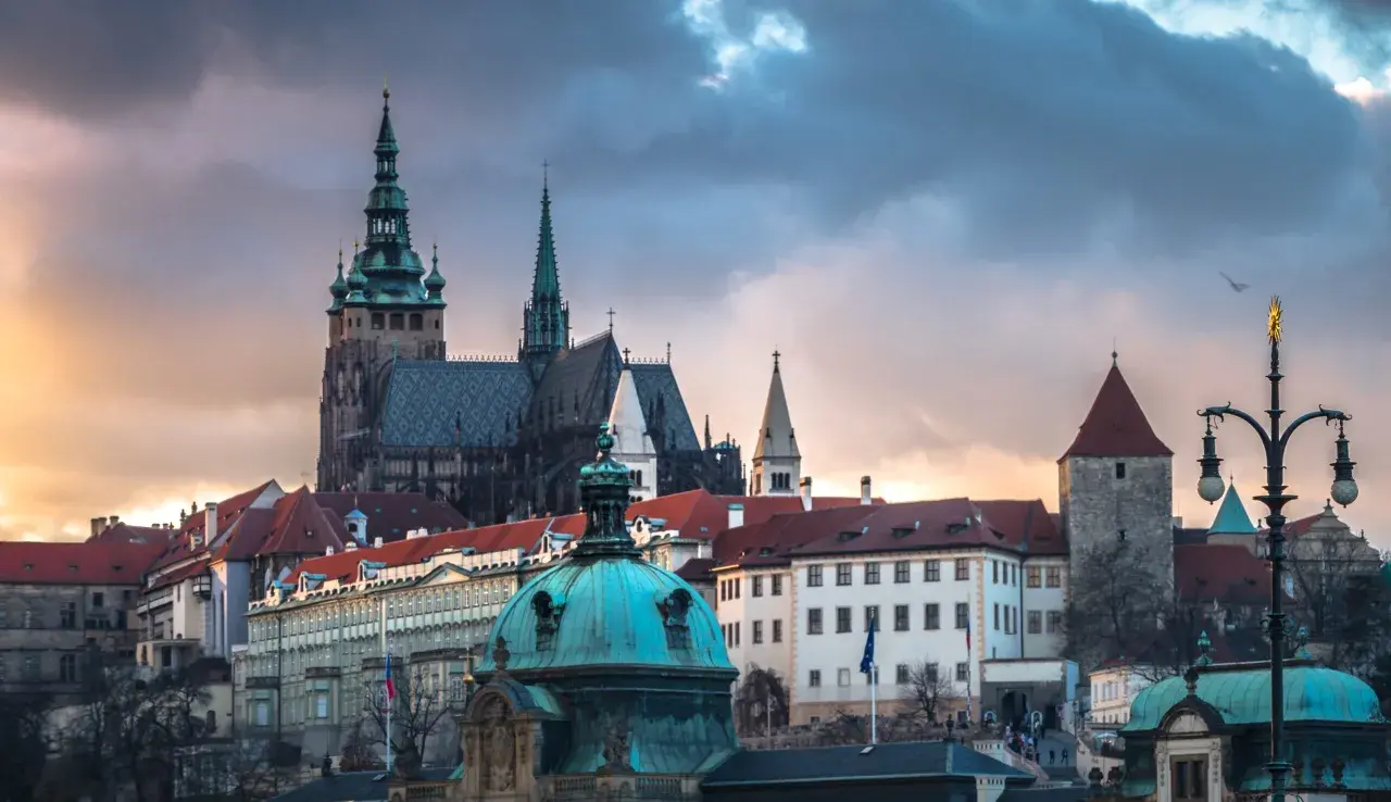 Prag dom mit seinen Türmen und Dächern unter dramatischem Himmel. Ein Vogel fliegt über die historische Kulisse.