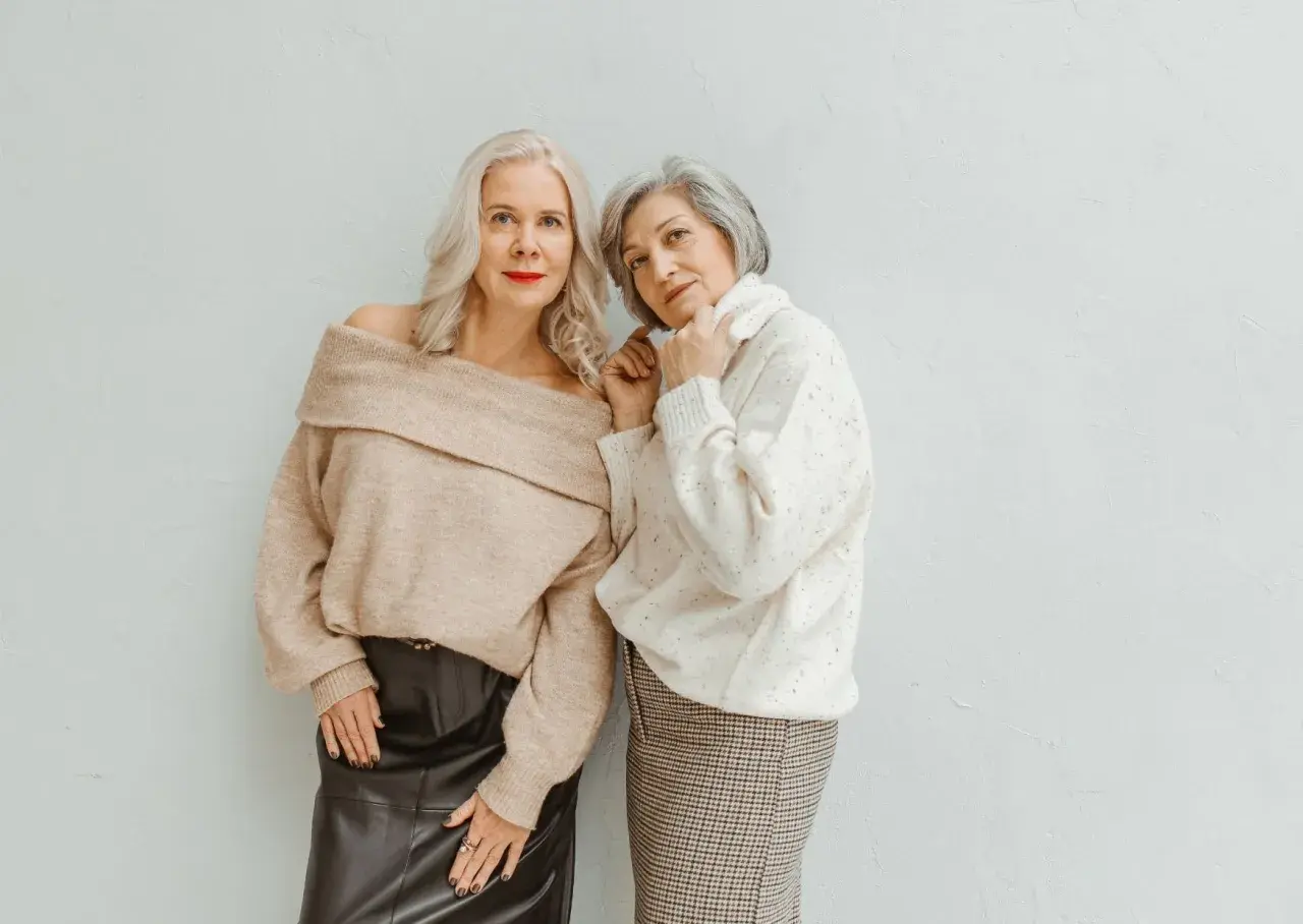Deux femmes élégantes, l'une en pull beige dénudant ses épaules et jupe en cuir, l'autre en pull blanc et jupe à carreaux, prouvent qu'il n'y a pas d'erreurs de style qui vieillissent.
