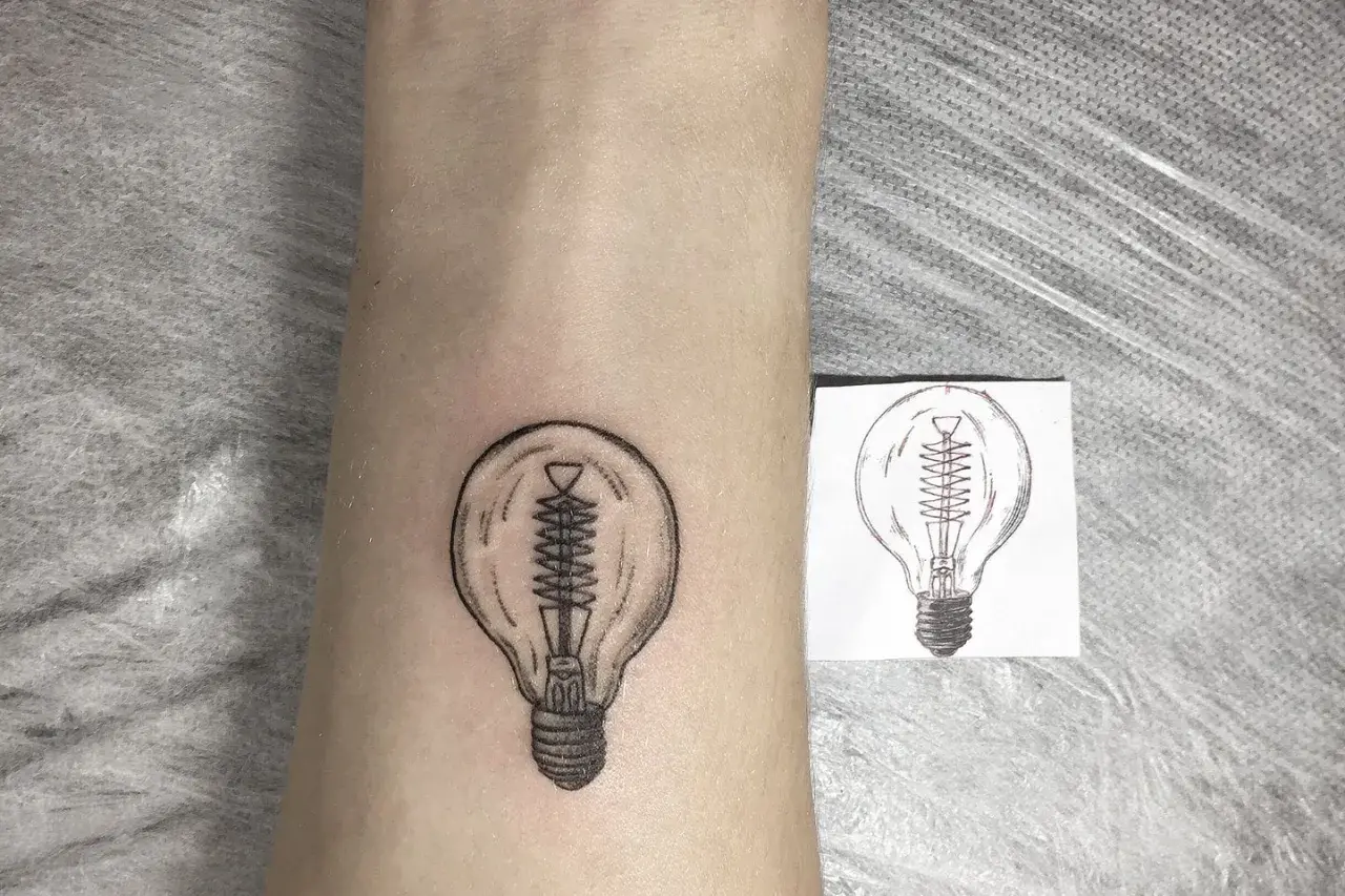 Nowy tatuaż żarówka na skórze, obok szkicu. Symbol pomysłu i światła.