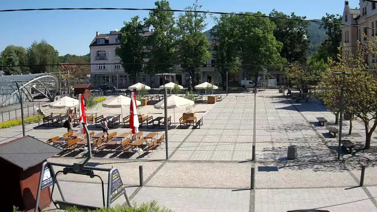 Letni dzień na rynku w Ustroniu. Puste stoliki kawiarniane czekają na gości, a słońce rzuca cienie na brukowany plac.