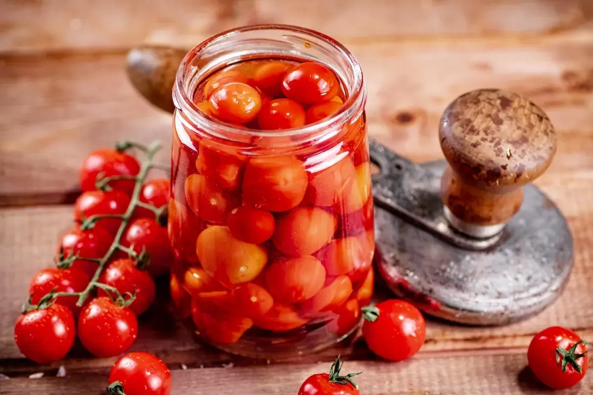 Glas voller Tomaten, bereit zum Einkochen wie Oma. Frische Kirschtomaten und ein Einkochgerät auf Holzuntergrund.