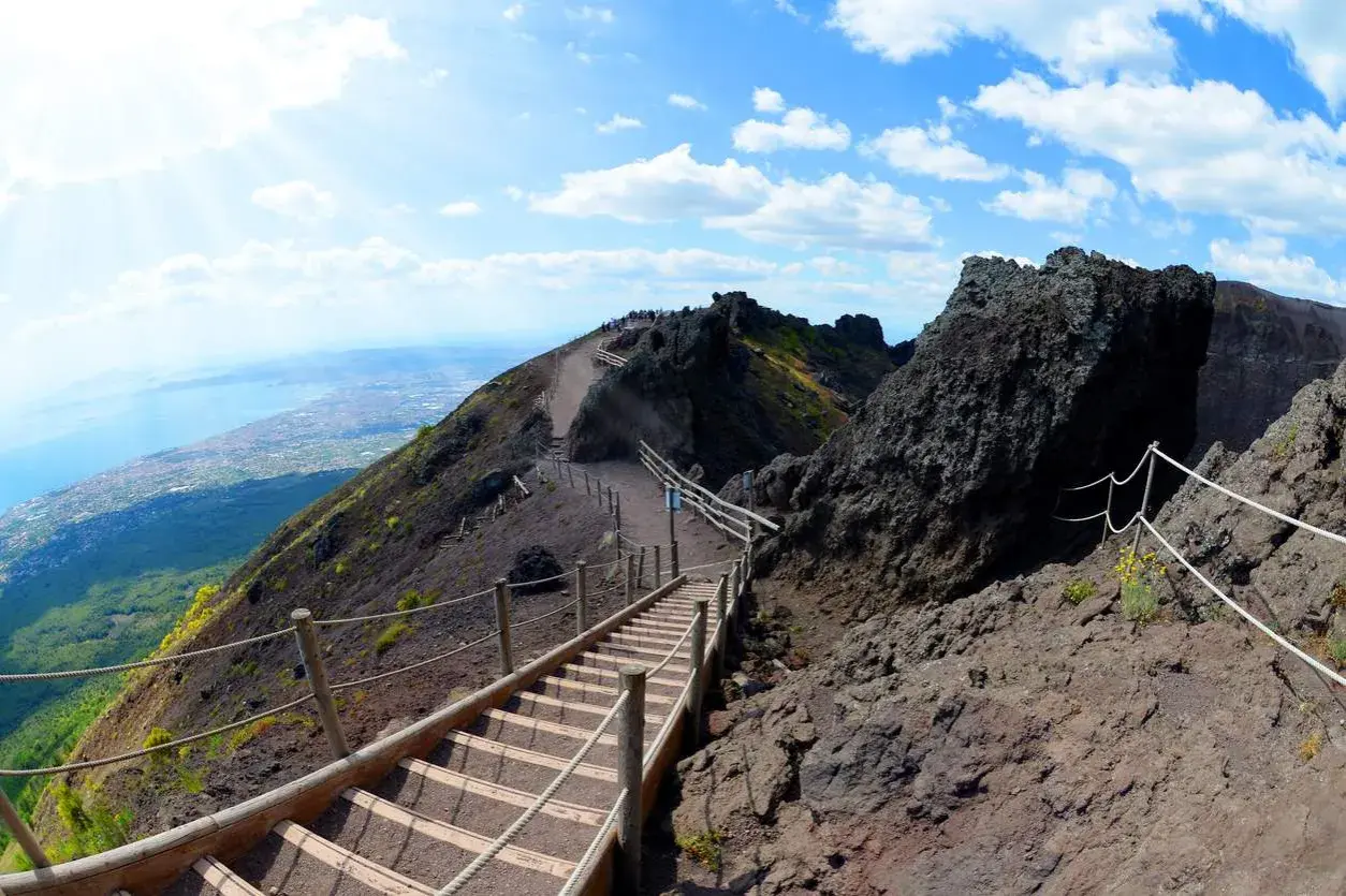Sentiero sul cratere del Vesuvio, un vulcano attivo. Scale di legno e corde guidano i visitatori verso la cima, con vista sul golfo.