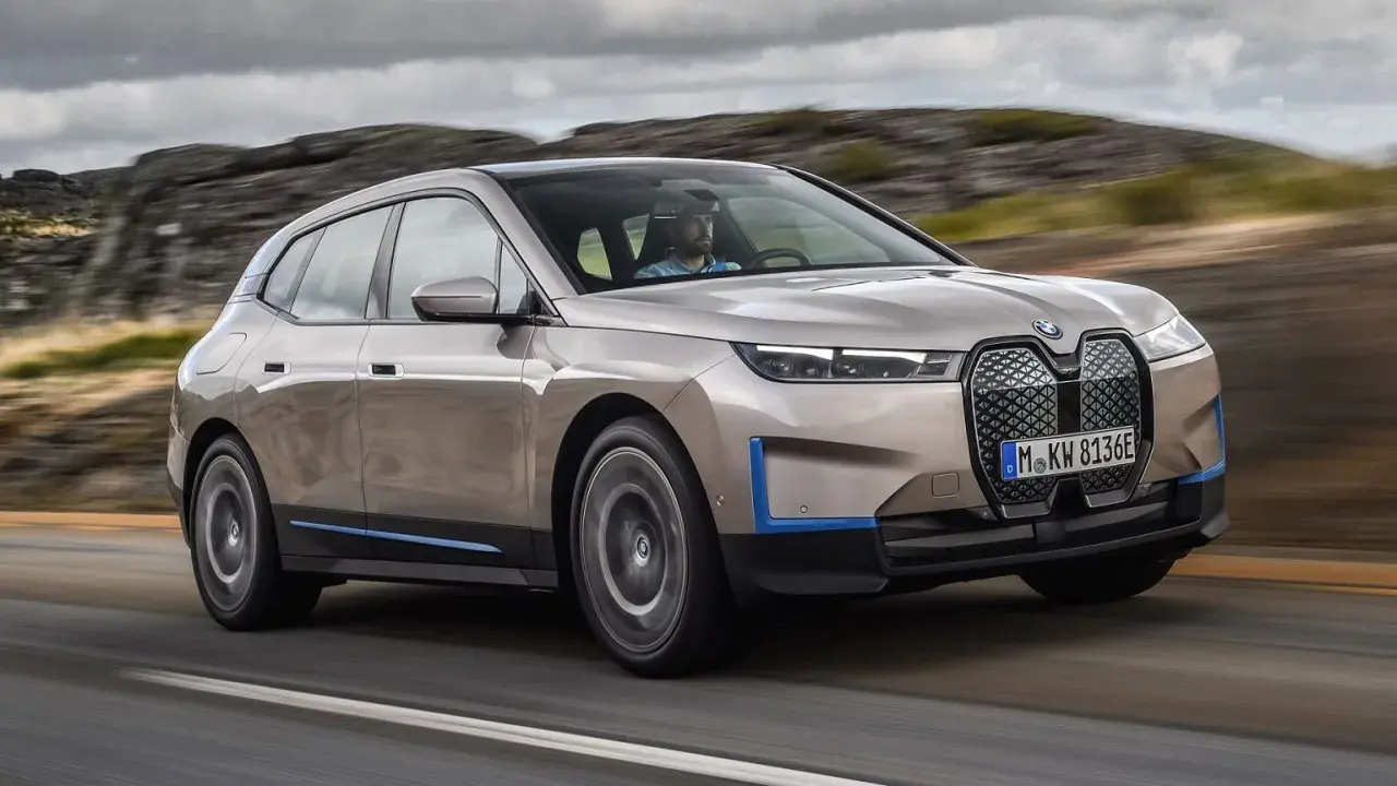 Złoty BMW iX jedzie po drodze, otoczony skalistym krajobrazem.