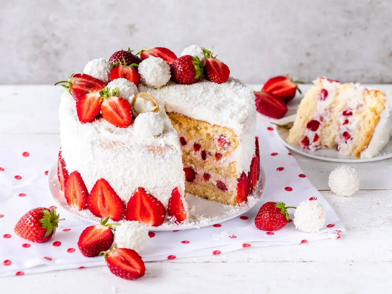 Eine köstliche Erdbeer Raffaello Torte, umhüllt von Kokosraspeln und dekoriert mit frischen Erdbeeren und Raffaello Kugeln.