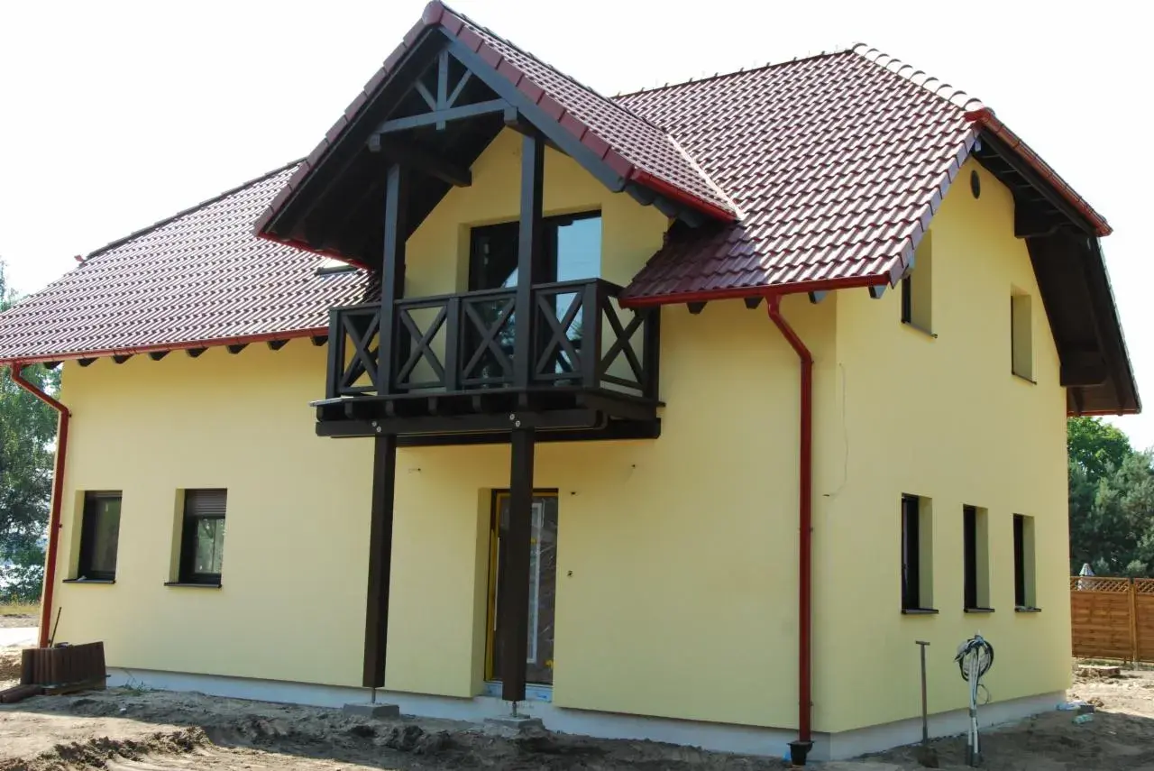 Jasnożółty dom z czerwonym dachem i drewnianym balkonem.