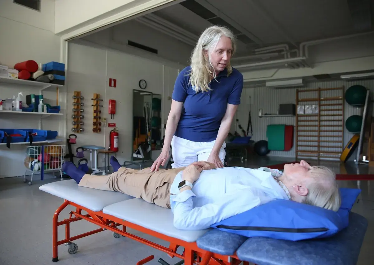 Fysioterapeut undersöker en patient som ligger på en brits. Patienten verkar vara fixerad bebis i sin position, redo för behandling.