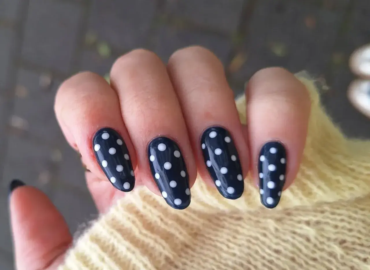 Manucure élégante avec un nail art pois sur fond bleu marine. Les ongles sont ornés de petits ronds blancs, créant un look ludique et chic.