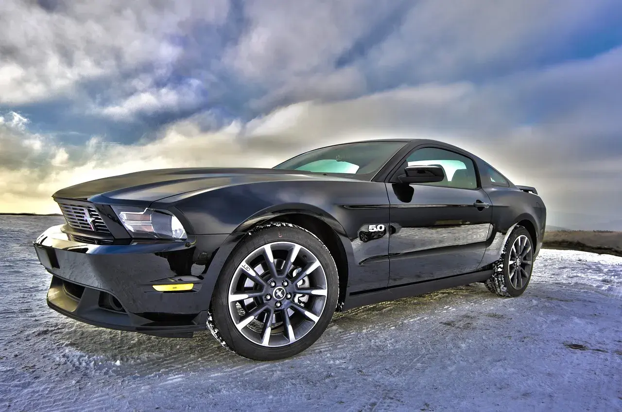 Czarny Ford Mustang GT 5.0, jeden z tych tanich sportowych aut, zaparkowany na zaśnieżonej drodze pod dramatycznym niebem.