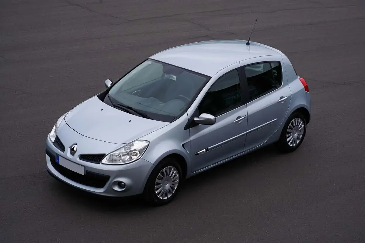 Vue aérienne d'une Renault Clio 3 argentée, modèle à injection, garée sur un sol asphalté.
